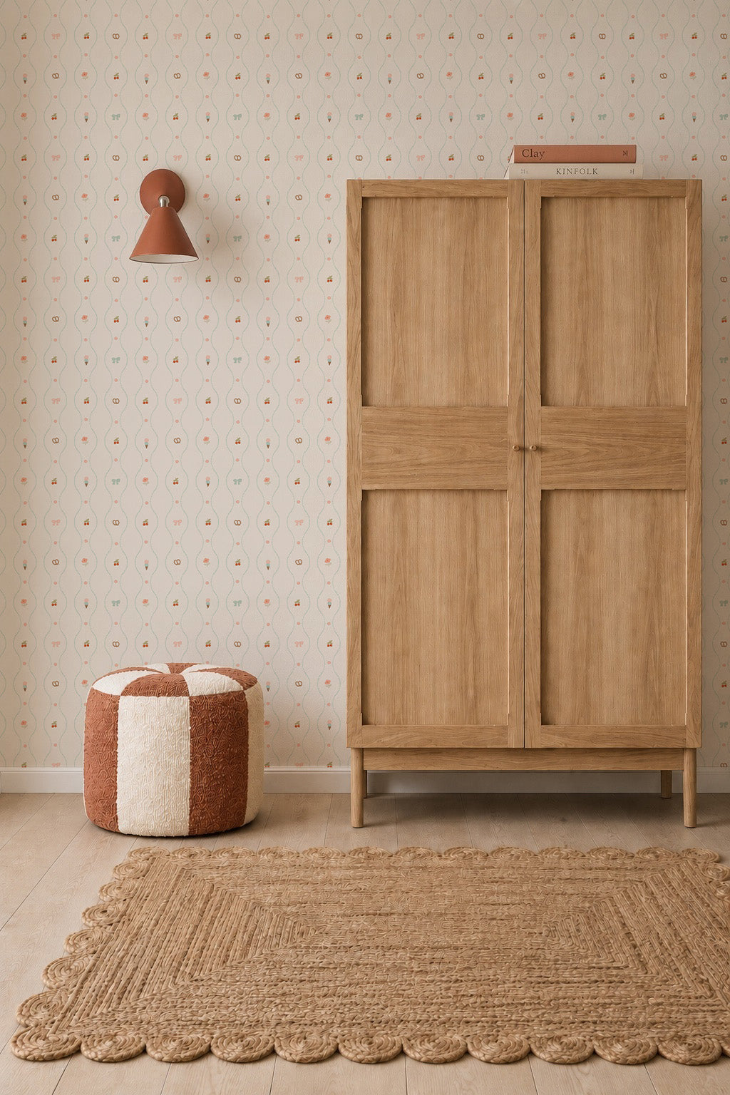 Minimalist room with a wooden wardrobe, woven rug, red and white pouf, wall lamp, and books on top of the wardrobe. The nursery is adorned with Little Patisserie Stripe Wallpaper, adding a gentle touch to the space.