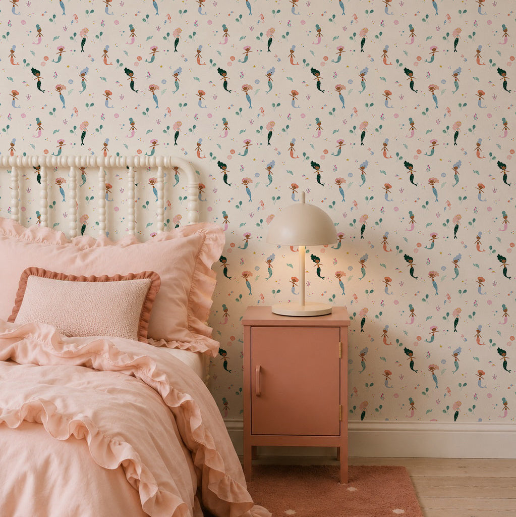 A cozy bedroom featuring Mermaid Friends Wallpaper, a ruffled pink bedspread with matching pillows, and a pink nightstand topped with a round lamp for a charming, playful look.