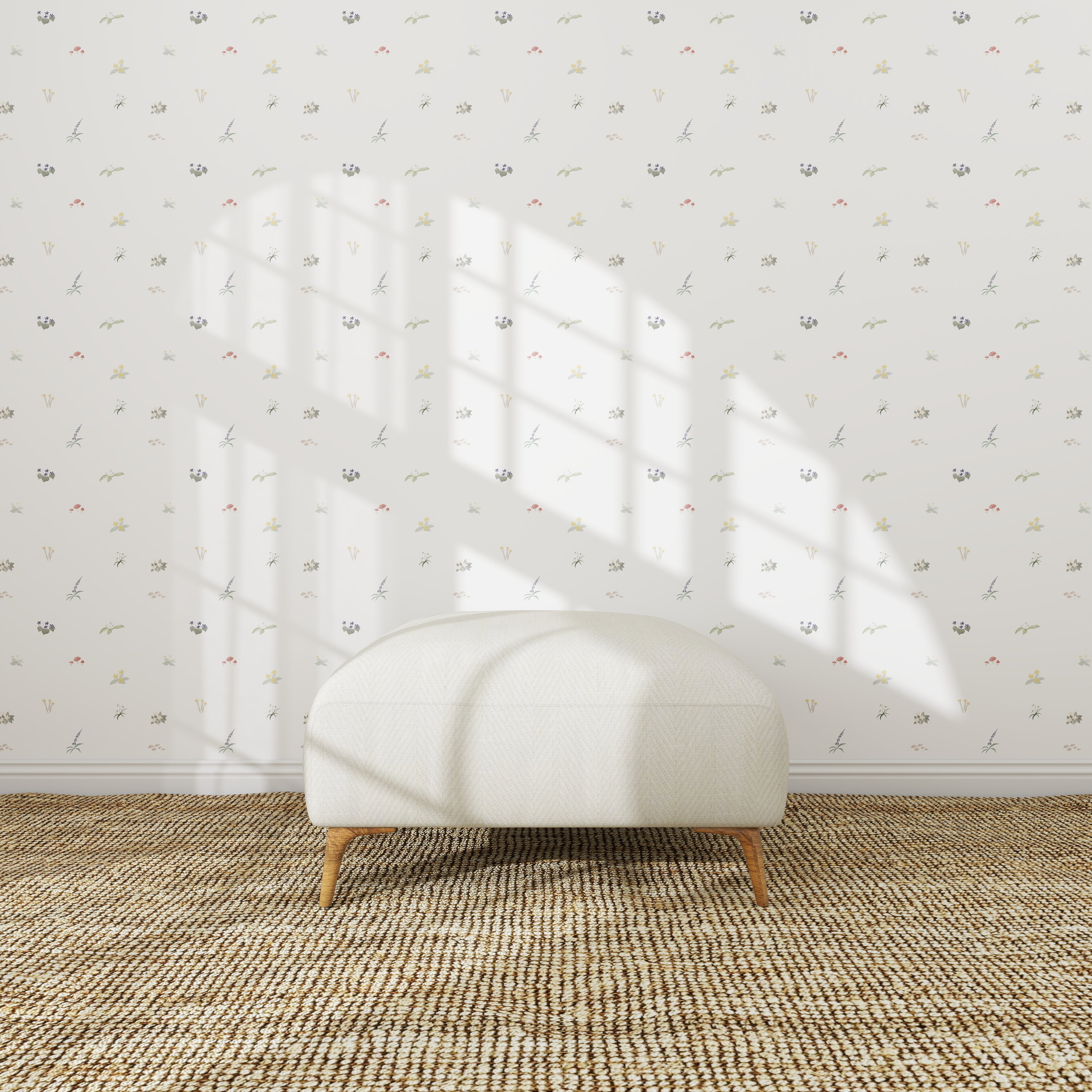 A simple white ottoman sits on a woven rug in front of a white wall adorned with Mollys Flower Garden Wallpaper Repeat | Sample. Sunlight streams in, casting a window-shaped shadow above the ottoman.