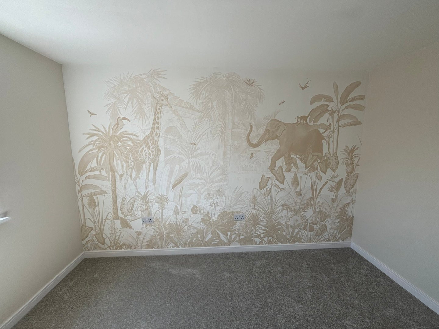 The Magic Jungle Wallpaper Mural showcases jungle animals like giraffes and elephants among tropical plants in neutral beige, ideal for a childs room with grey carpet and cream walls.