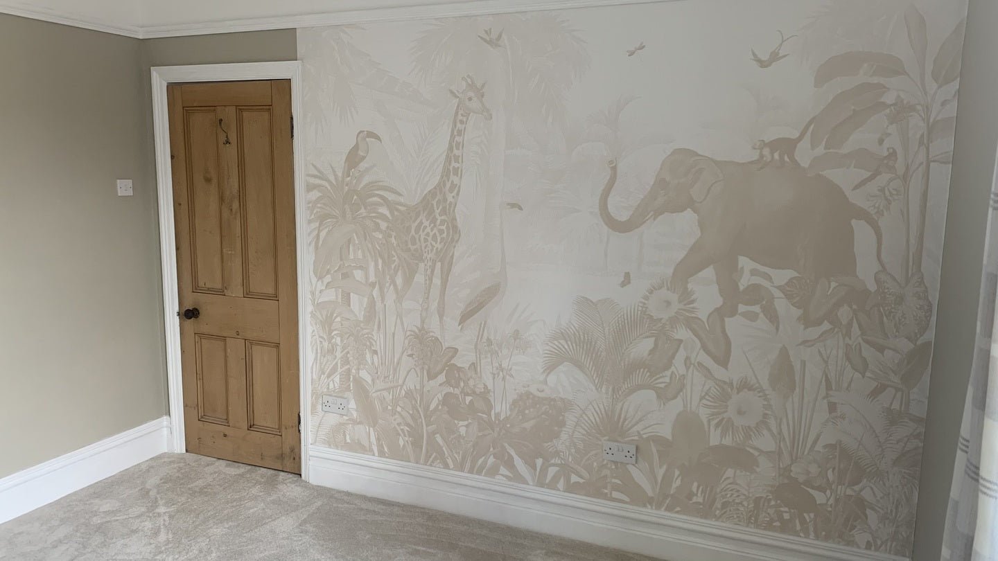 The Magic Jungle Wallpaper Mural, in beige tones with a giraffe, elephant, birds, and tropical plants, decorates one wall of a childrens room featuring light carpet, white trim, and a wooden door.