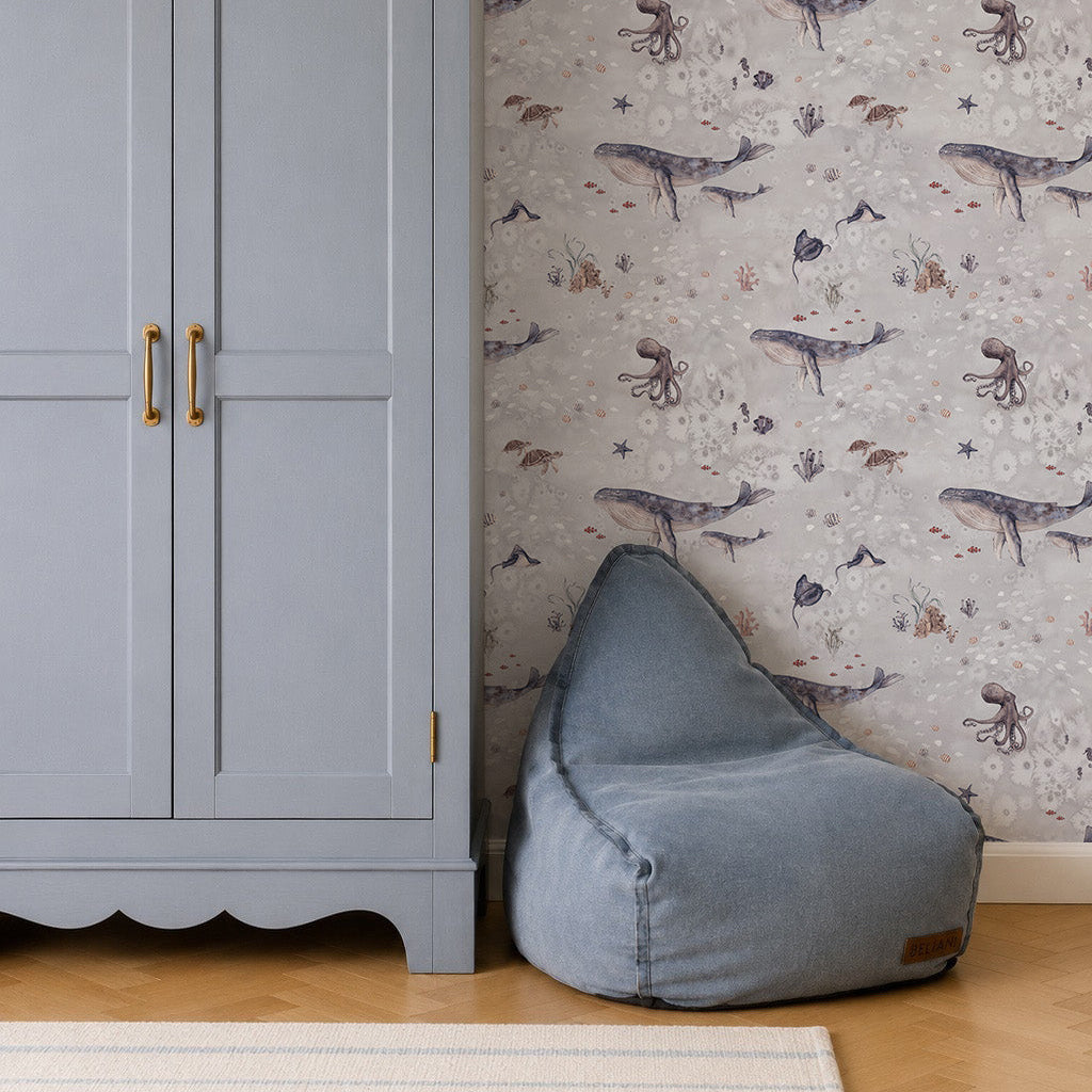 A pale blue wardrobe with gold handles stands next to a light blue bean bag chair. The wall behind them features Ocean Friends Wallpaper, ideal for children&