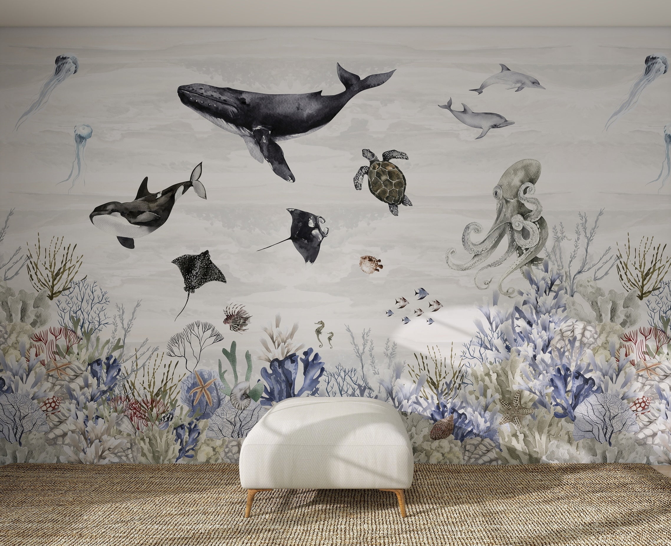 A white ottoman sits on a woven rug in front of the Ocean Magic Mural, Watercolour, featuring illustrated ocean animals like a whale, orca, turtle, rays, octopus, and fish swimming above vibrant coral and sea plants.