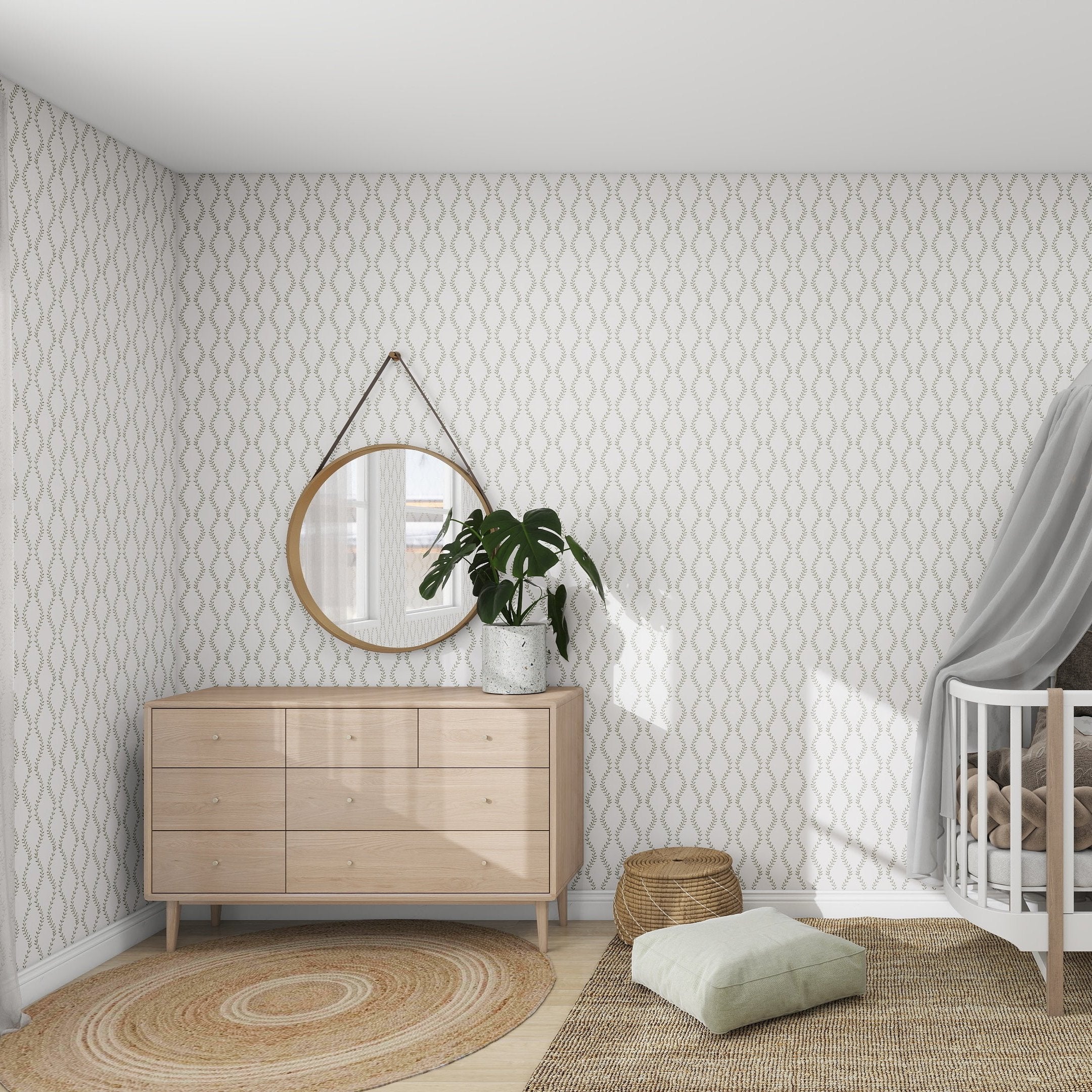 The nursery showcases the Vintage Vines Wallpaper Repeat Pattern by munks and me, a wooden dresser with a plant and round mirror, and a crib with a curtain. A woven rug and cushions adorn the wooden floor, while gentle light from the window adds elegance to the room.