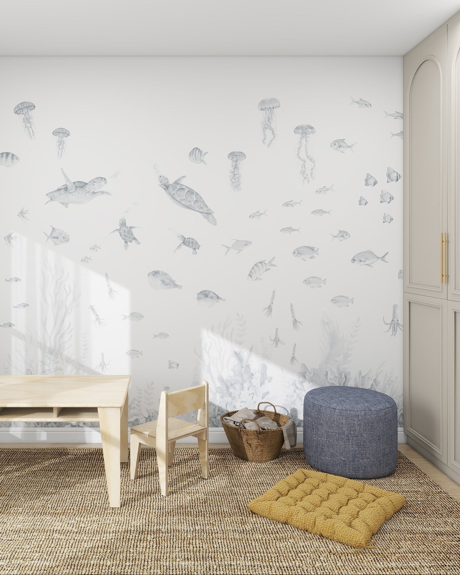Bright children’s room featuring a Fish Tank Mural, Blue underwater-themed wallpaper, plus a small wood table and chairs, cubby shelf, blue pouf, yellow cushion, large closet with gold handles, sheer curtains, wicker basket, and jute rug on a light floor.