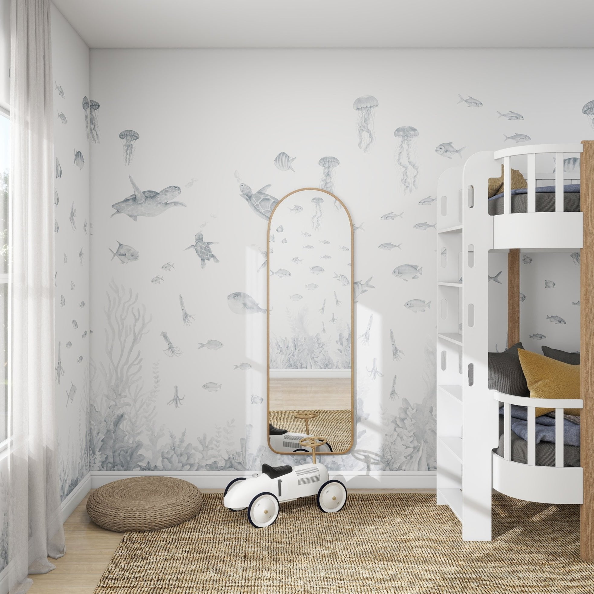 A childrens room features a white bunk bed and toy car on wooden flooring. The walls display the Fish Tank Wallpaper Mural | Blue by munks and me, with sea life like fish and jellyfish. A tall arched mirror leans against the wall, while a round woven rug adds charm to the cozy space.