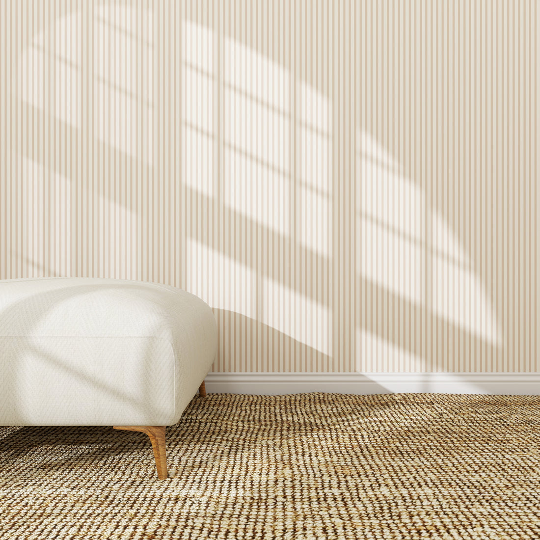 A minimalist room features Pico Stripe Wallpaper Rose | Sample, sunlight streaming in, a woven natural fiber rug, and a white upholstered bench with wooden legs in the left corner.
