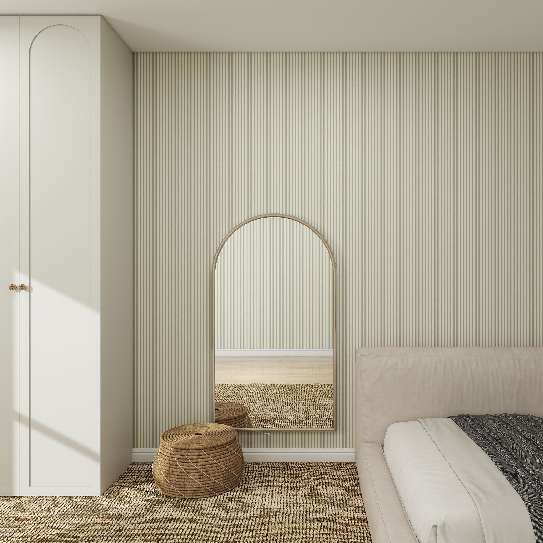A minimalist bedroom features a light-colored bed, woven round ottoman, arched mirror on Pico Stripe Wallpaper Green, built-in white wardrobe, and a textured woven rug on the floor.