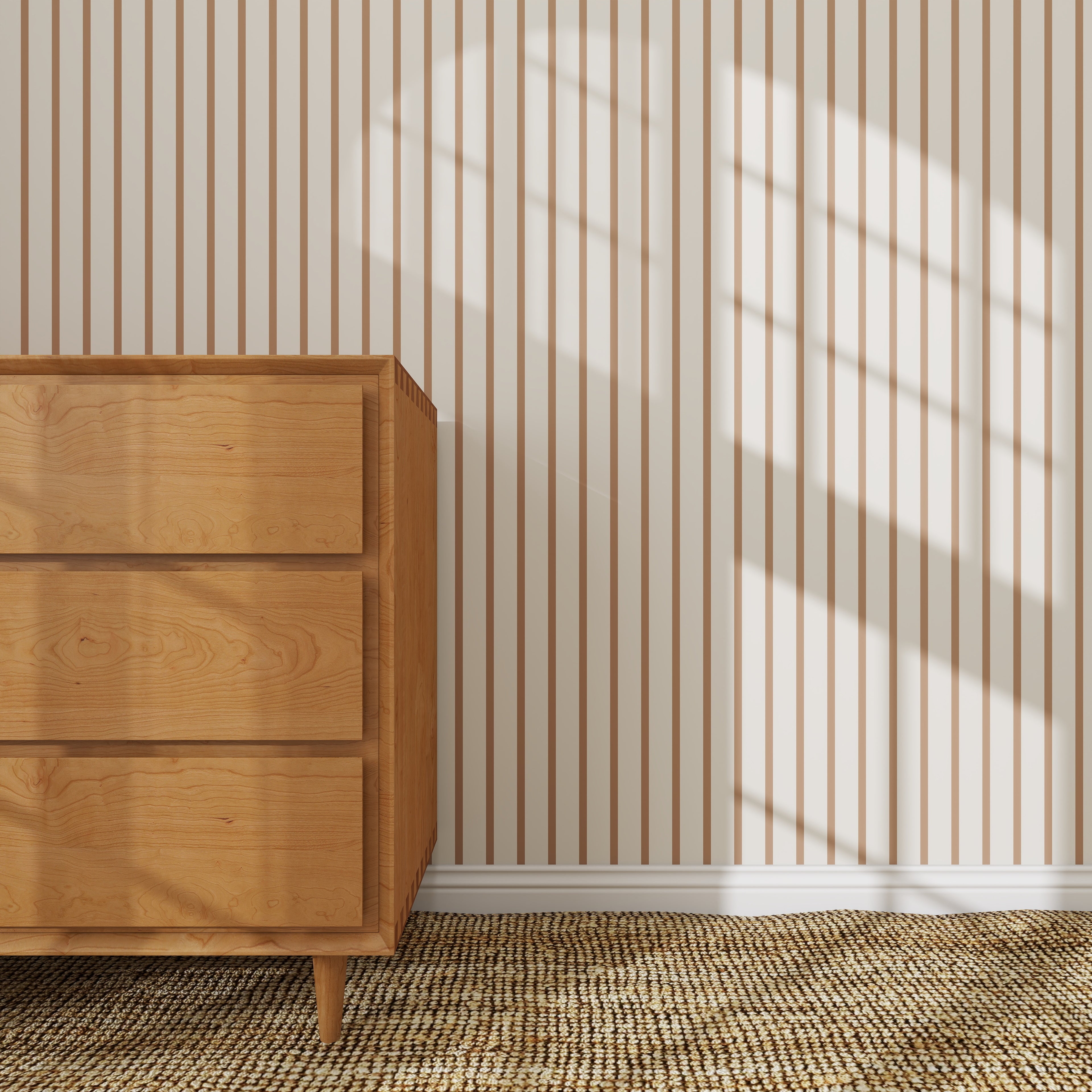 A wooden dresser sits on a woven rug against a wall decorated with Pinstripe Wallpaper Sample, Latte. Sunlight from a window casts a large grid-shaped shadow, highlighting the wallpaper’s excellent quality.
