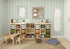 The childrens playroom includes a wooden table and chairs, storage cubbies with books and bins, and a pegboard for crafts. The Jolly Jester Wallpaper in vibrant green adds color, while a framed motivational quote elevates the ambiance. A cushioned mat and basket complete the cozy setup.