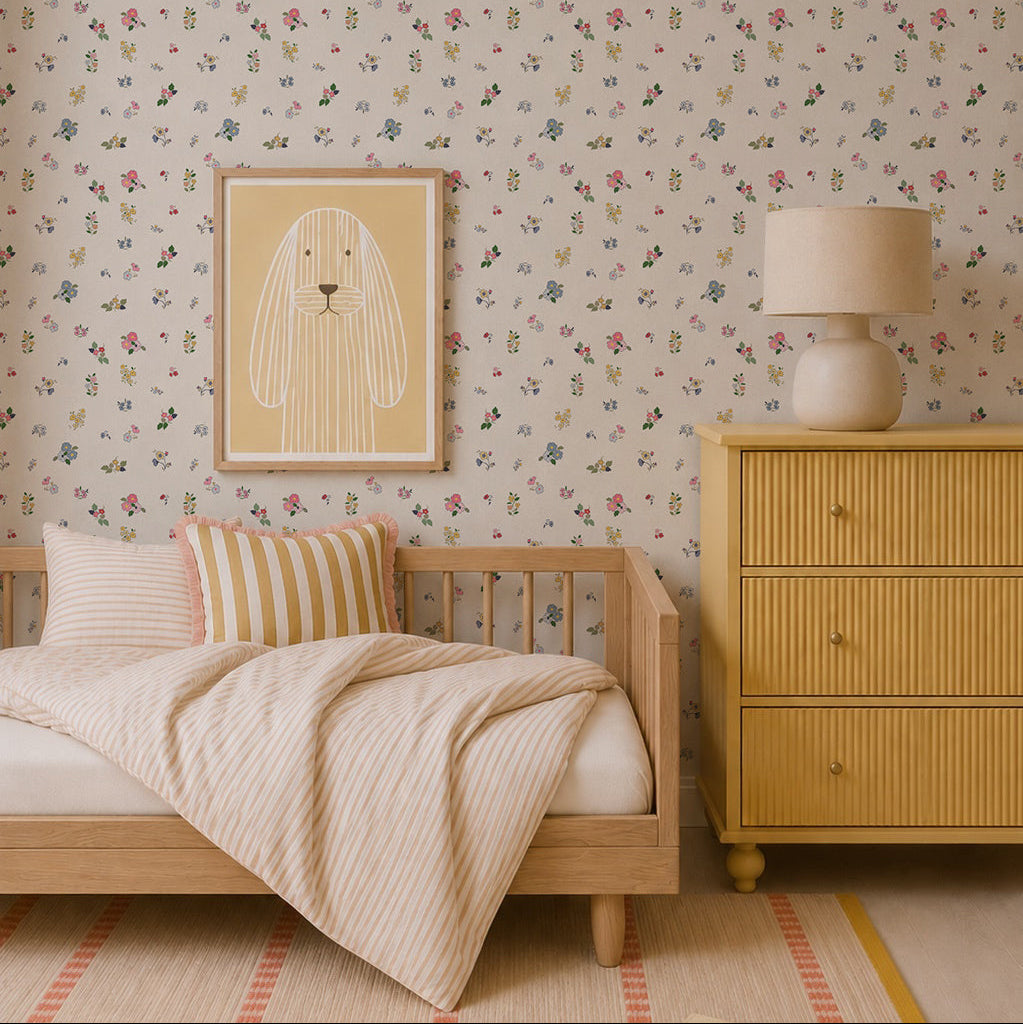 A cozy children’s bedroom features Powdered Petals Wallpaper, a wooden bed with striped bedding, a yellow dresser, matching lamp, and a framed bunny illustration in soft neutral and pastel tones.