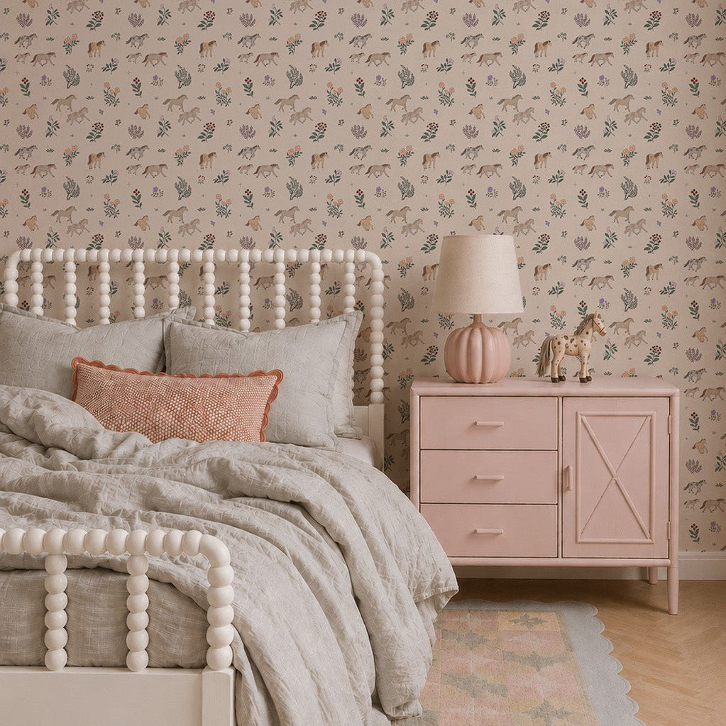 A cozy bedroom features a white spindle bed with gray bedding, a pink pillow, and a pink nightstand topped with a pink lamp and animal figurines. The walls are adorned with Quincy Horses Wallpaper in soft pastel colors for a delicate touch.