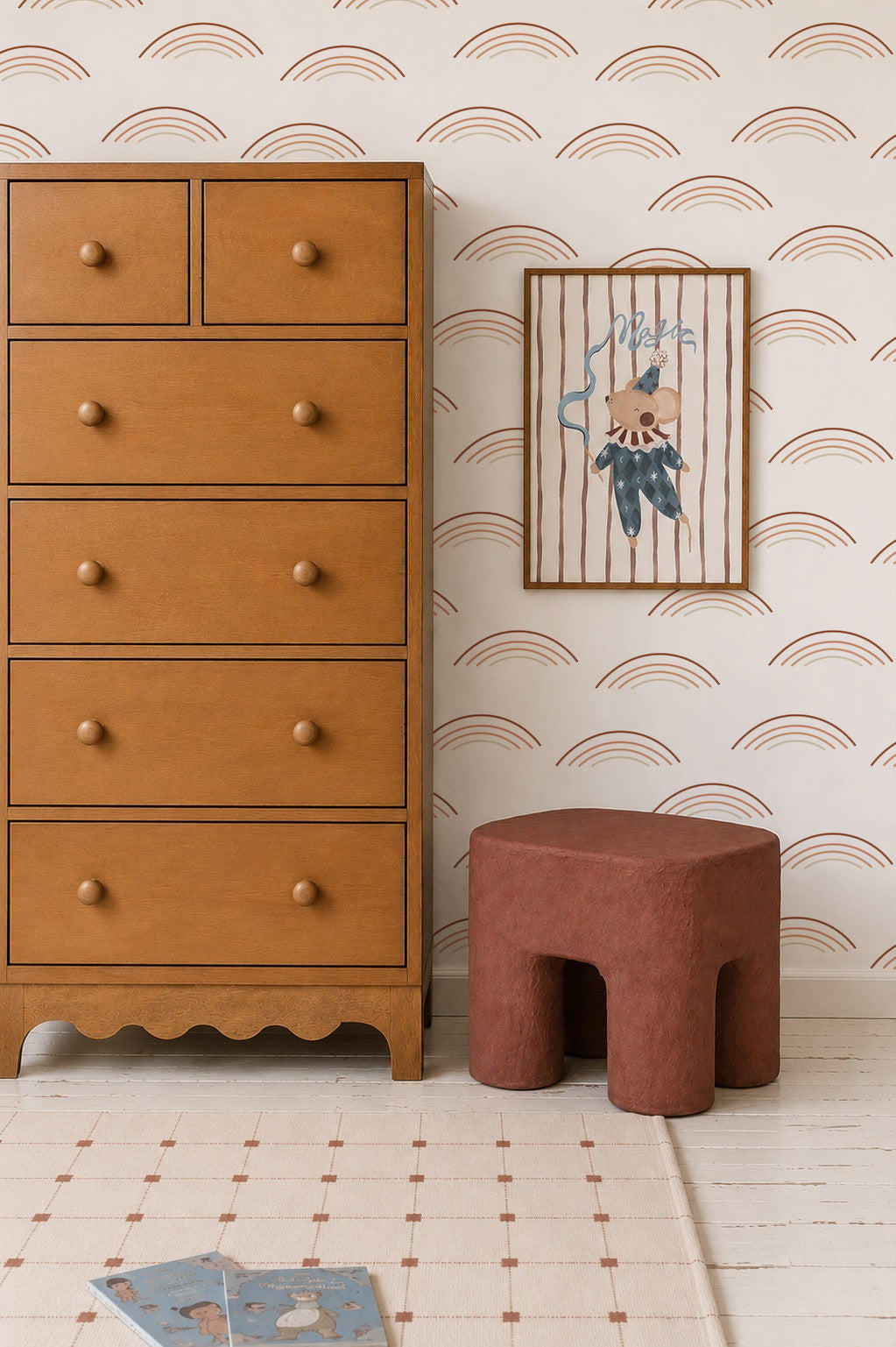 A wooden dresser stands beside a small, brown stool and a framed bear picture on a striped background. The wall features Rainbow Wave Wallpaper in rust tones, and a children&