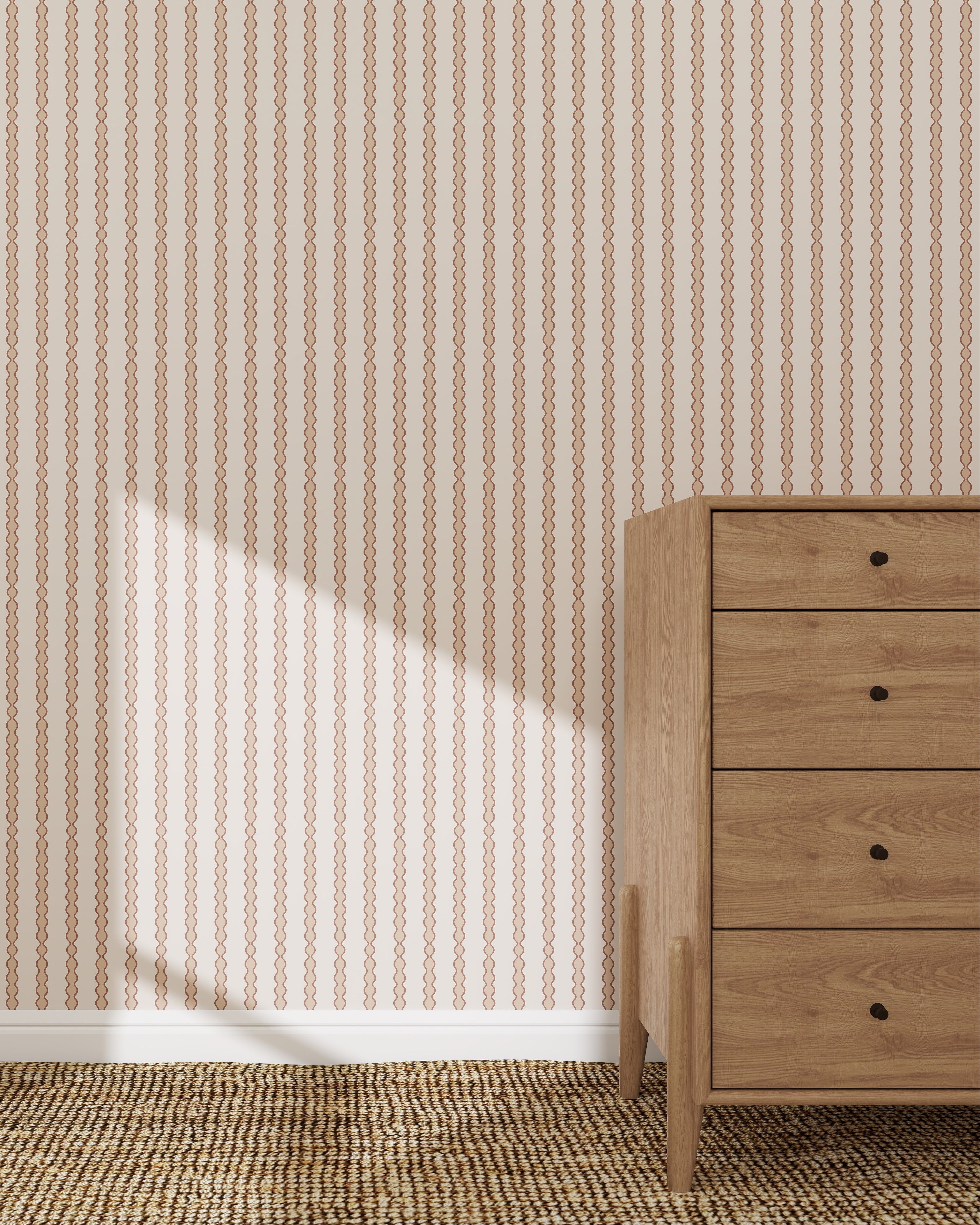 A wooden dresser with five drawers sits on a woven carpet beside a wall adorned with Little Abacus Stripe Wallpaper Sample in Rose. Sunlight casts a triangular shadow, highlighting the elegant pattern and quality of the wallpaper.