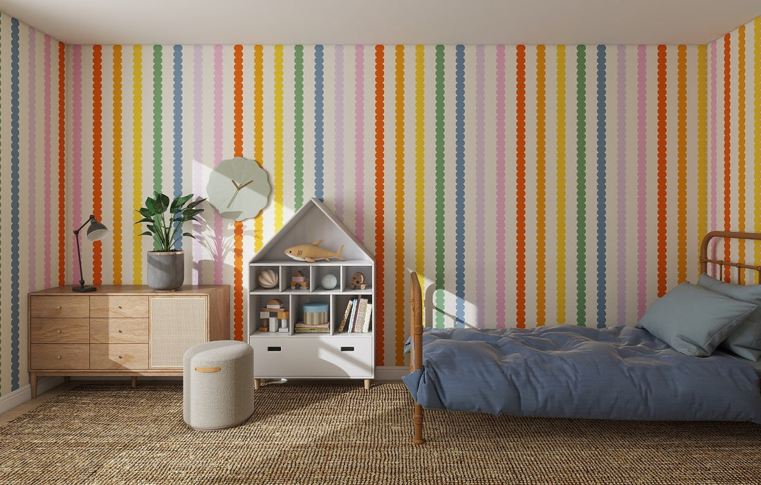 A colorful childrens room featuring the Scallop Stripe Wallpaper Repeat Pattern | Rainbow, a single bed with blue bedding, wicker rug, decorated dresser, small ottoman, and a house-shaped bookshelf filled with toys and books.