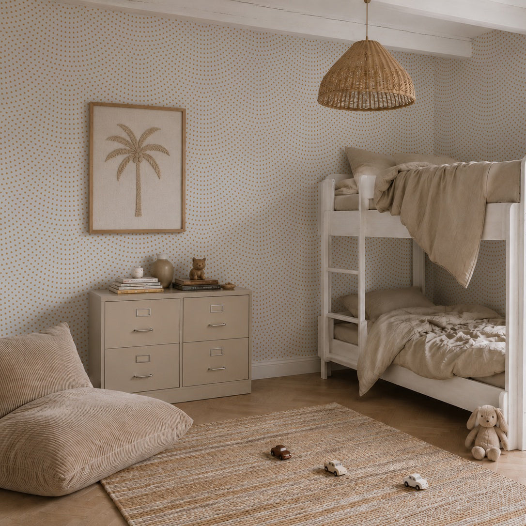 A neutral-toned kids’ bedroom features bunk beds, a woven pendant lamp, a palm tree art piece, a cozy floor pillow, a rug, two toy cars, and a dresser adorned with plush toys. The subtle coastal nursery decor theme is beautifully highlighted by the gentle touch of the Scallop Shell Mural in Mustard. Soft elements like nursery wallpaper and seaside accents create a calm and cozy atmosphere in the room.