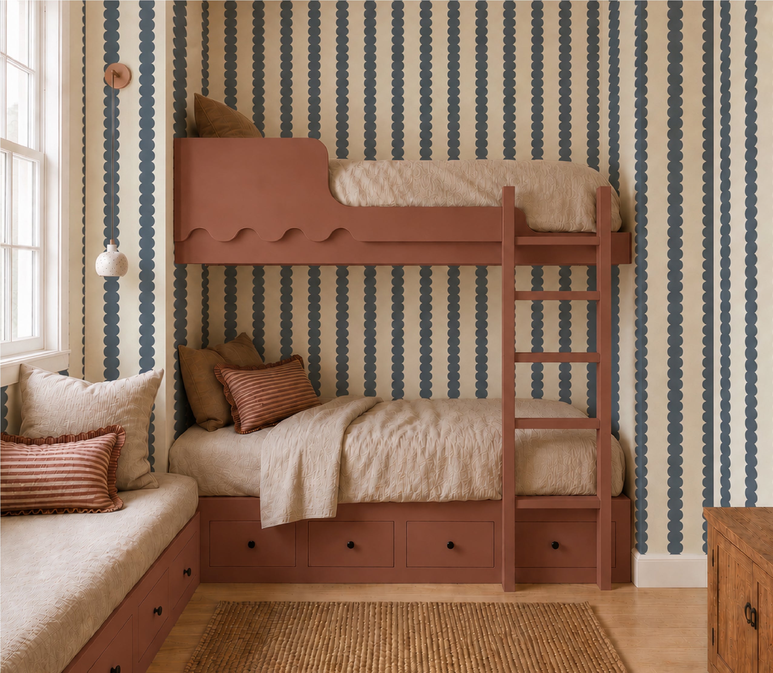 A cozy bedroom features rust-colored bunk beds with built-in drawers, beige bedding, and striped pillows. A window seat sits nearby while Scallop Stripe Wallpaper Sample in Deep Blue adds wavy blue and cream stripes to the walls.
