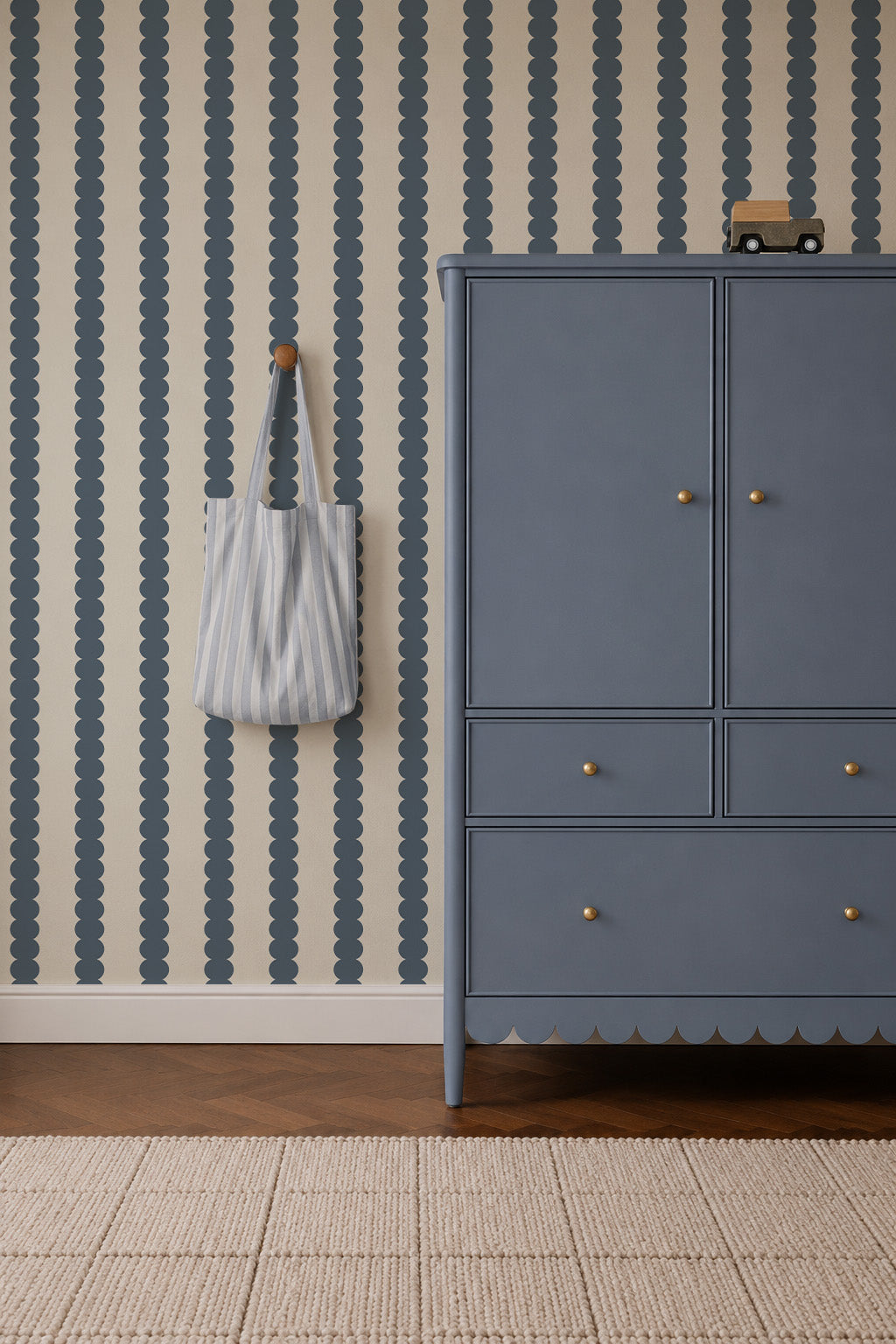 Scallop Stripe Wallpaper, Deep Blue features vertical scalloped patterns on a cream background, positioned next to a blue cabinet with a striped tote bag hanging on the wall.