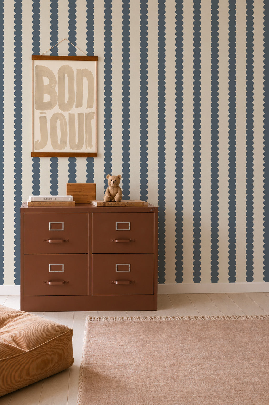 Scallop Stripe Wallpaper, Deep Blue serves as a backdrop for a brown four-drawer cabinet, a teddy bear, and a framed Bonjour print.