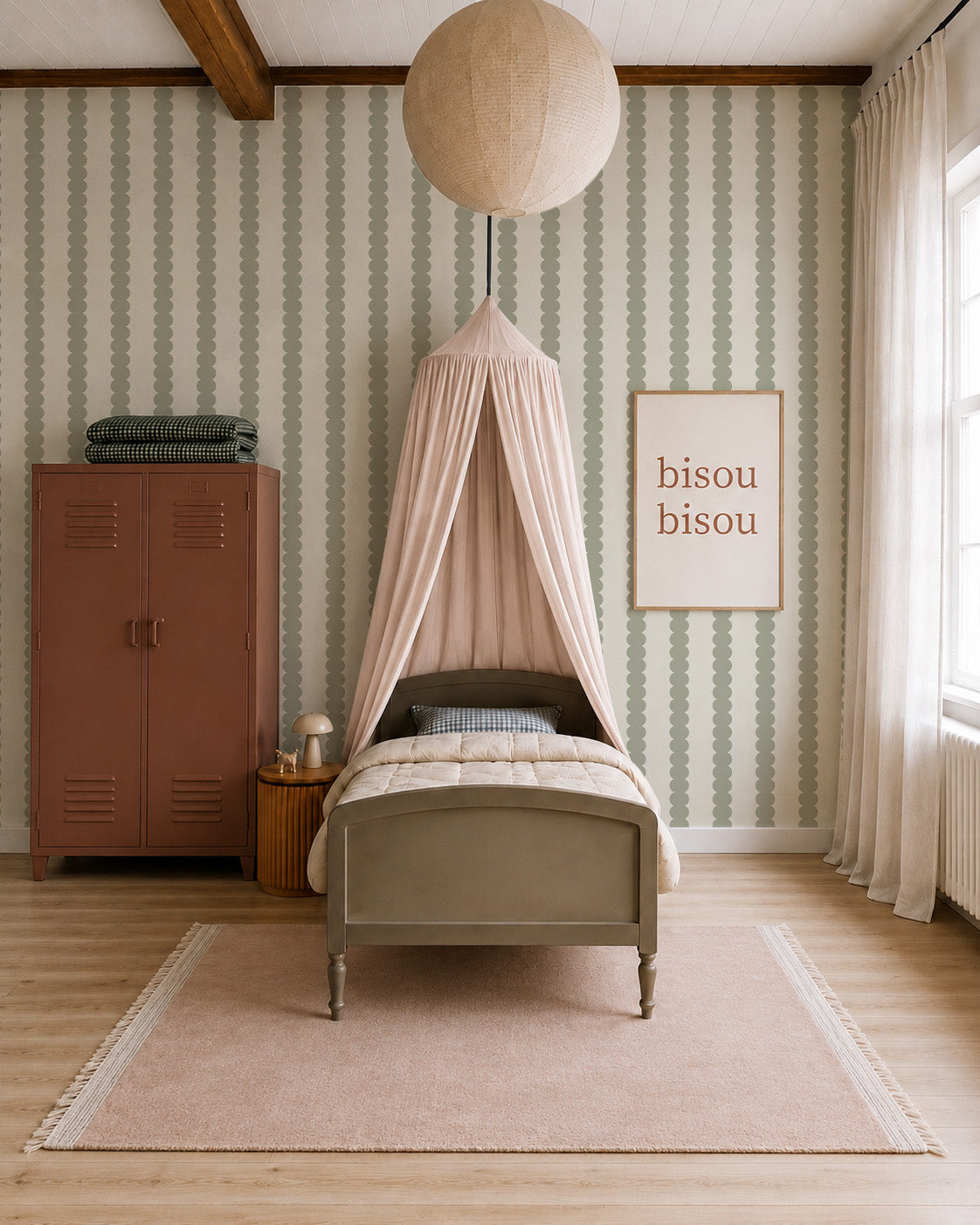 A cozy kids bedroom features a metal bed under a pink canopy, a pink rug, a mauve locker, stacked blankets, a globe lamp, large windows, and a framed bisou bisou print on walls adorned with Scallop Stripe Wallpaper in Green.
