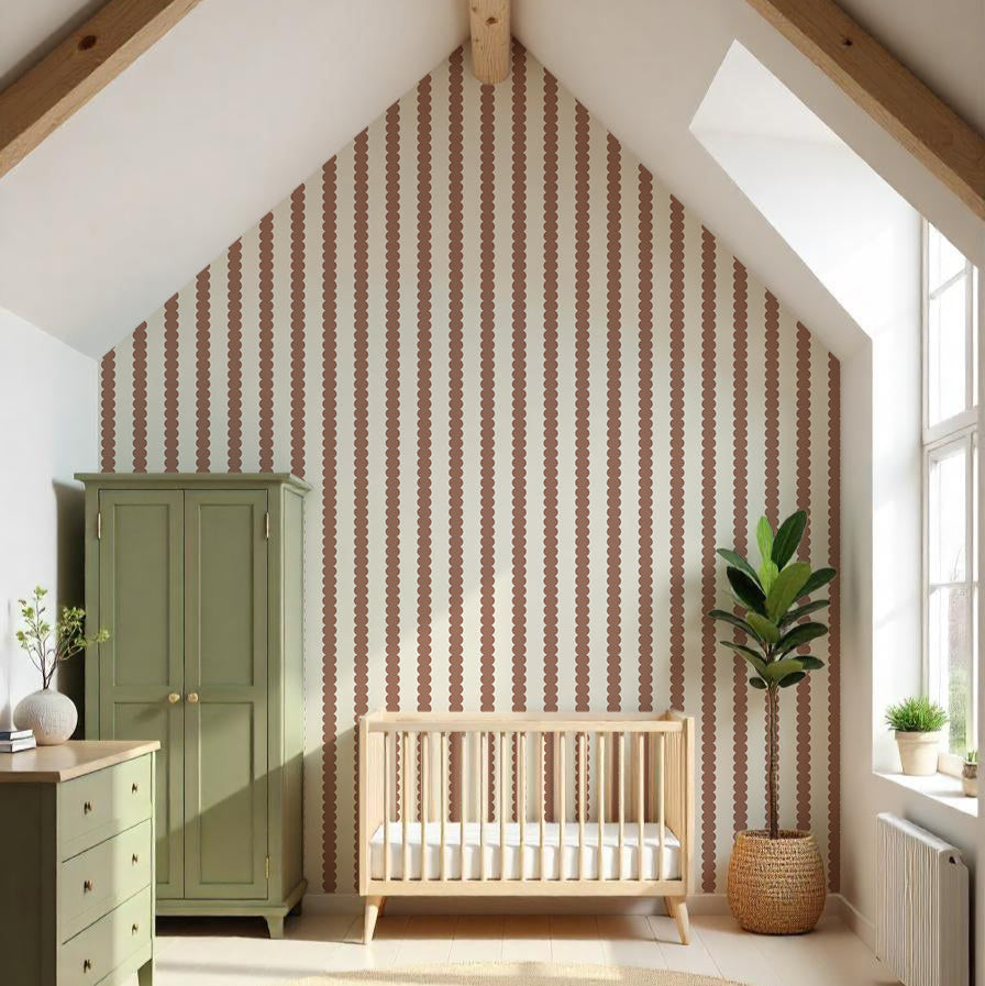 A cozy nursery features a wooden crib under a vaulted ceiling. The walls are adorned with Scallop Stripe Wallpaper Mocha, adding color with brown and white stripes. A green wardrobe and dresser match the decor, while a potted plant and round woven rug sit on the wooden floor.