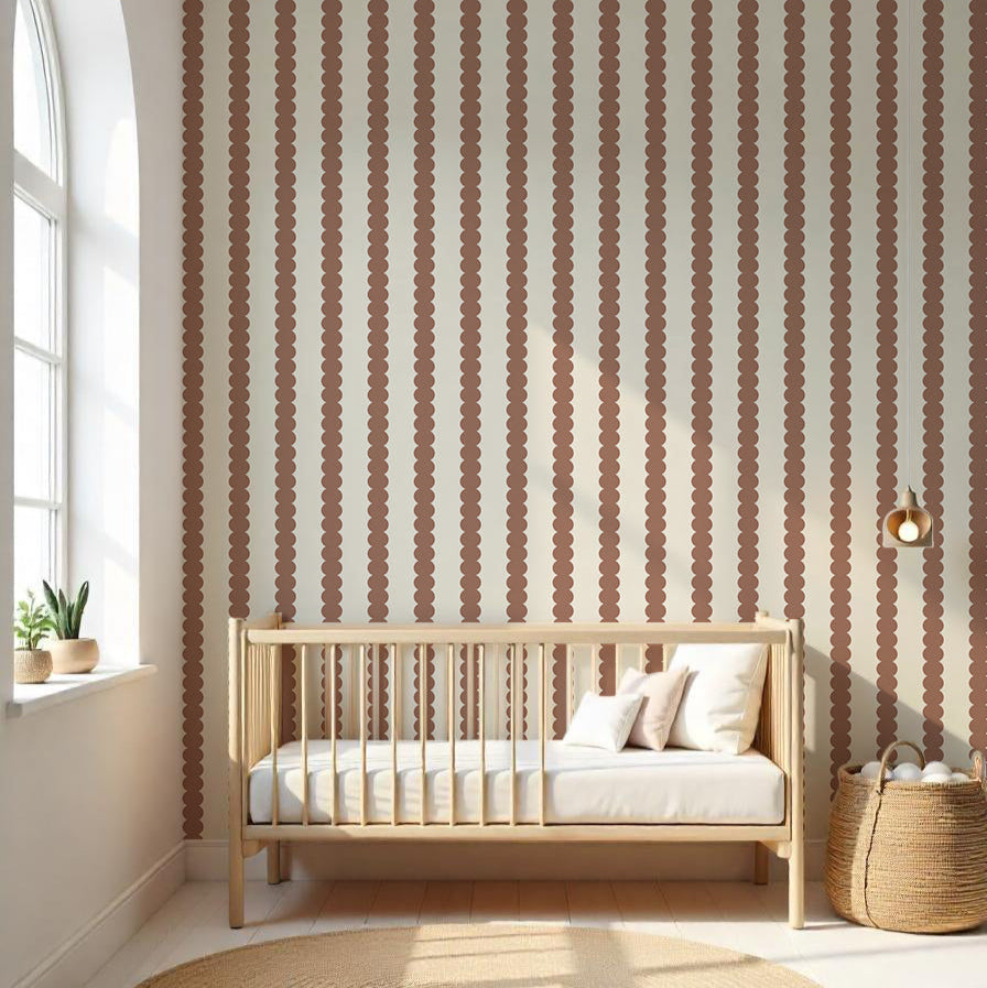 A minimalist nursery has a wooden crib with white bedding against a wallpapered wall featuring Scallop Stripe Wallpaper Mocha. Light from an arched window highlights a woven basket and round rug on the light wood floor, adding subtle pops of color to the serene space.