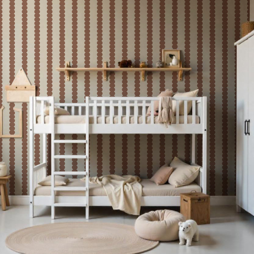 A cozy kids’ bedroom with white bunk beds, neutral bedding, a round rug, pouf, and toys features the Scallop Stripe Wallpaper Sample in Mocha above the beds, plus a wooden shelf for decor and vibrant color throughout.