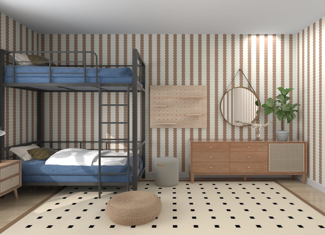 A cozy bedroom features a bunk bed with blue bedding, complemented by a wooden dresser and round mirror. A potted plant adds life alongside a pouf on a patterned rug. The Scallop Stripe Wallpaper Latte by munks and me enhances the rooms color and quality.