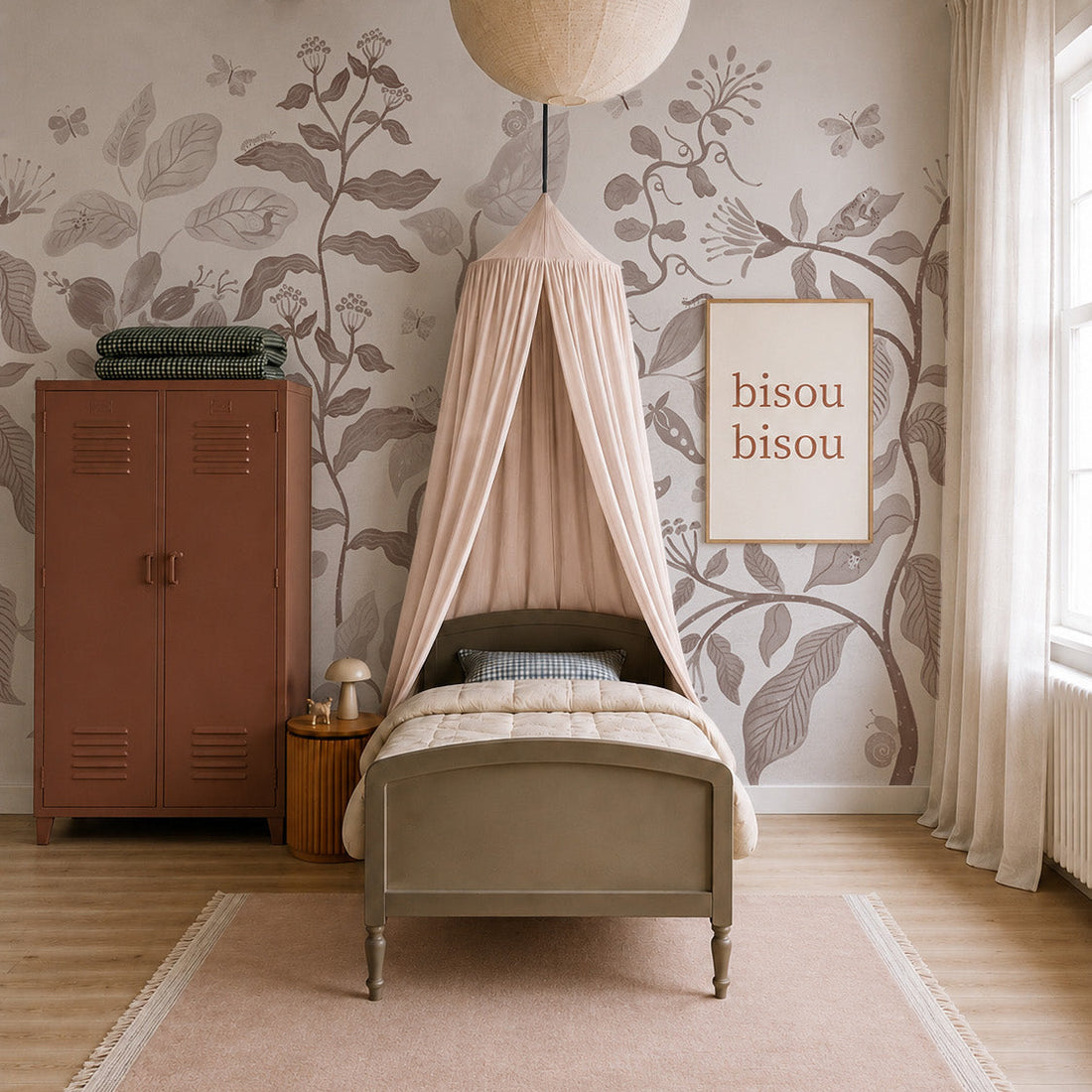 A cozy bedroom with a single bed under a pink canopy, Secret Garden Mural in Mocha, floral wallpaper, a brown locker, a lamp on a wooden nightstand, and a framed “bisou bisou” print. Soft light streams through large curtained windows.