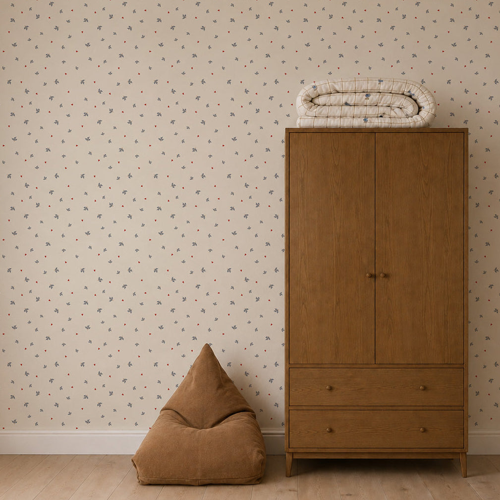 A brown bean bag sits next to a wooden wardrobe with two drawers, with a rolled-up blanket placed on top. The wall features Soaring Hearts Wallpaper, which has a light background and a small, subtle floral pattern.