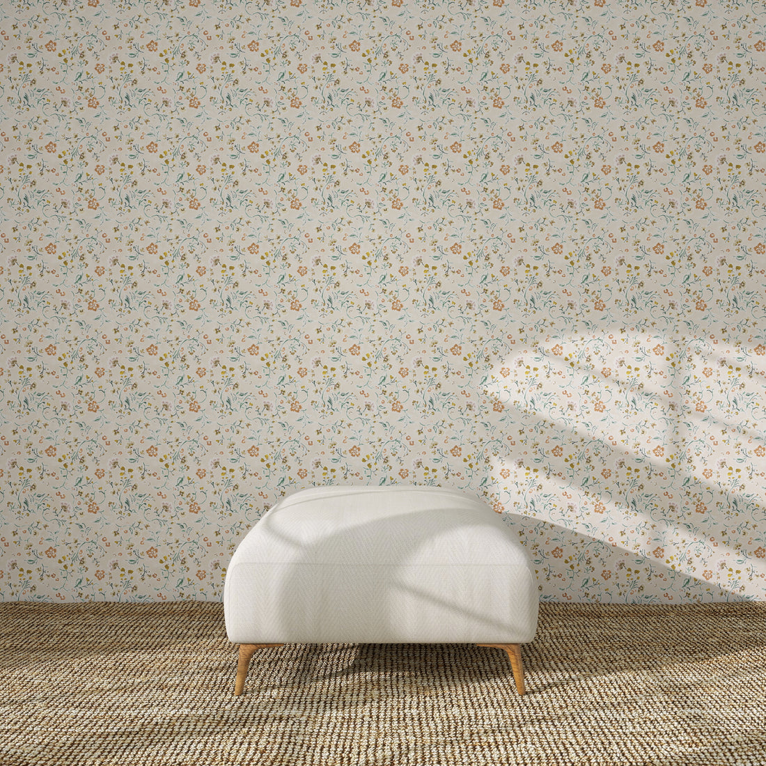 A white upholstered ottoman stands on a beige rug in front of Terra Bloom Wallpaper Sample. Sunlight casts shadows over the ottoman and accentuates the colour and floral design of the wallpaper.
