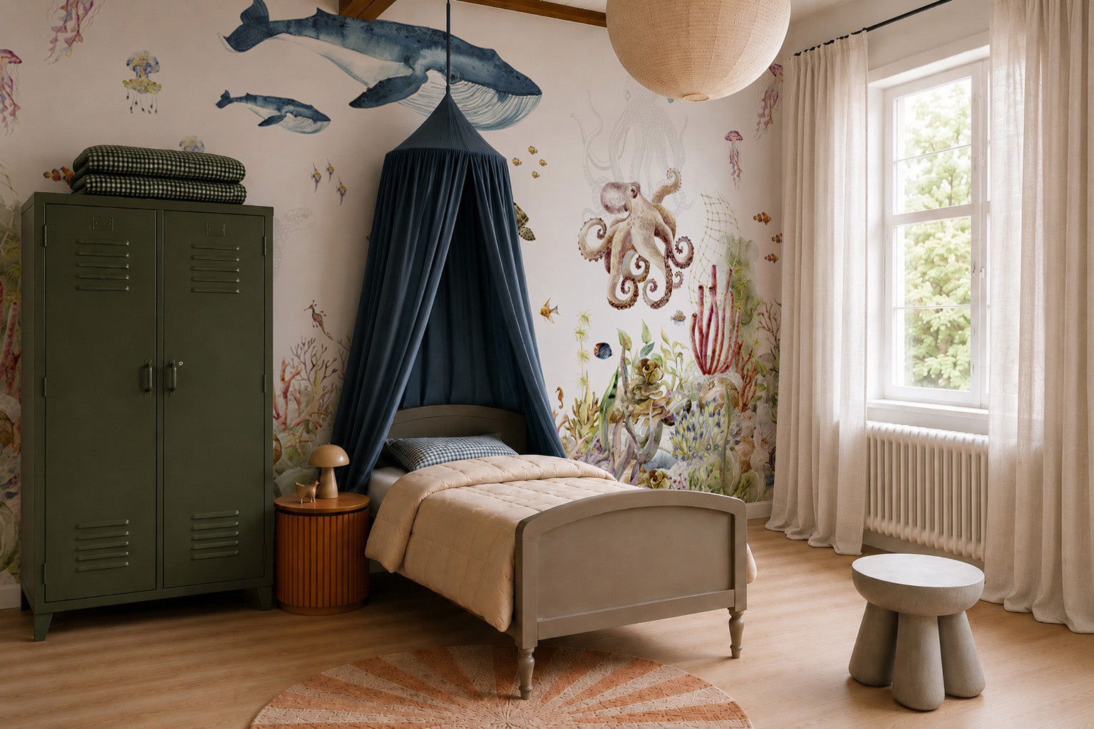 A cozy children’s bedroom designed especially for ocean lovers, featuring the vibrant Under The Sea Mural, Watercolour with playful sea creatures, a canopy bed, green wardrobe, round table, stool, and a window with sheer curtains letting in natural light.