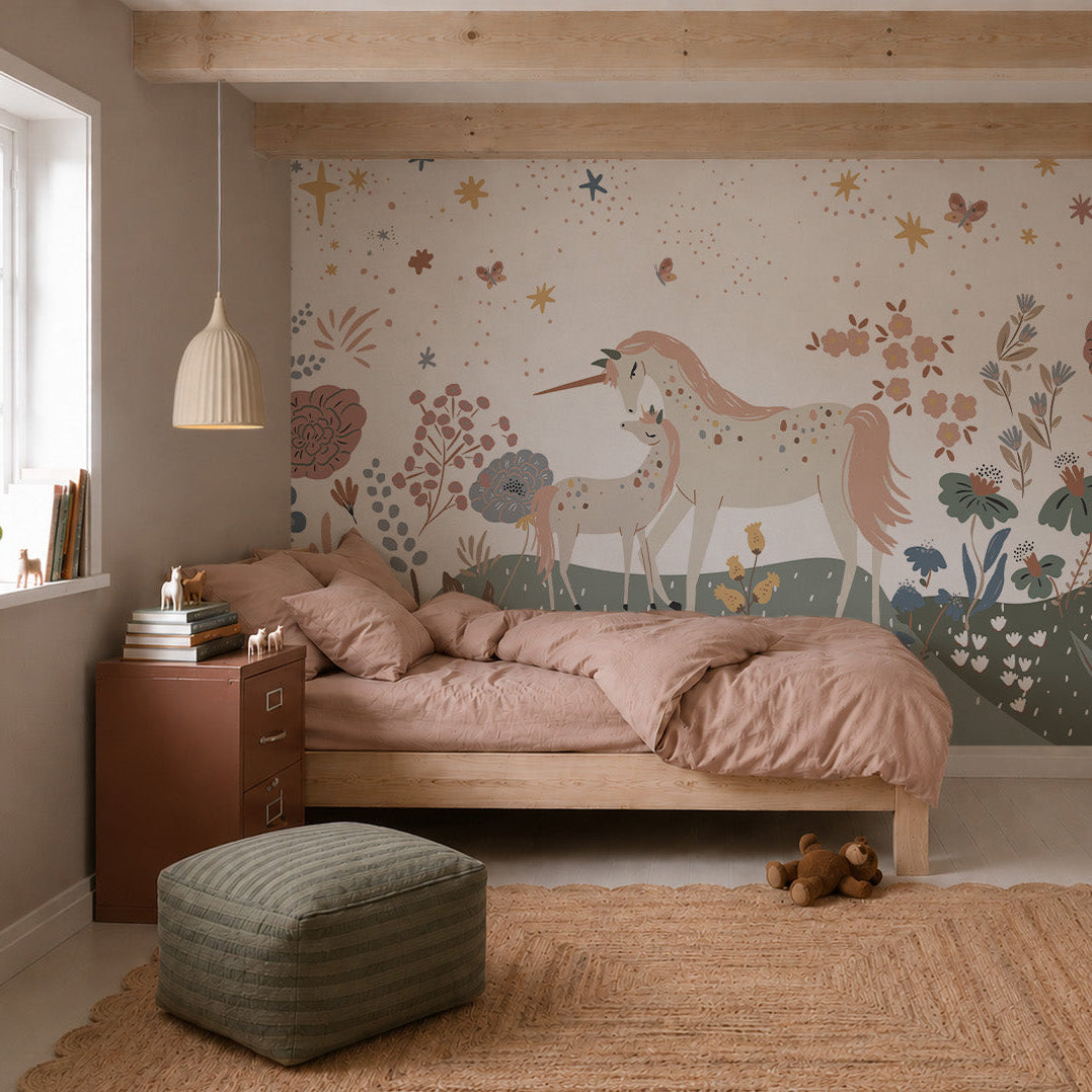 A cozy bedroom features a wooden bed, pink bedding, a jute rug, and the Unicorn Meadow Mural depicting two unicorns in a whimsical floral landscape. A green pouf, teddy bear, and natural light complete the inviting atmosphere.