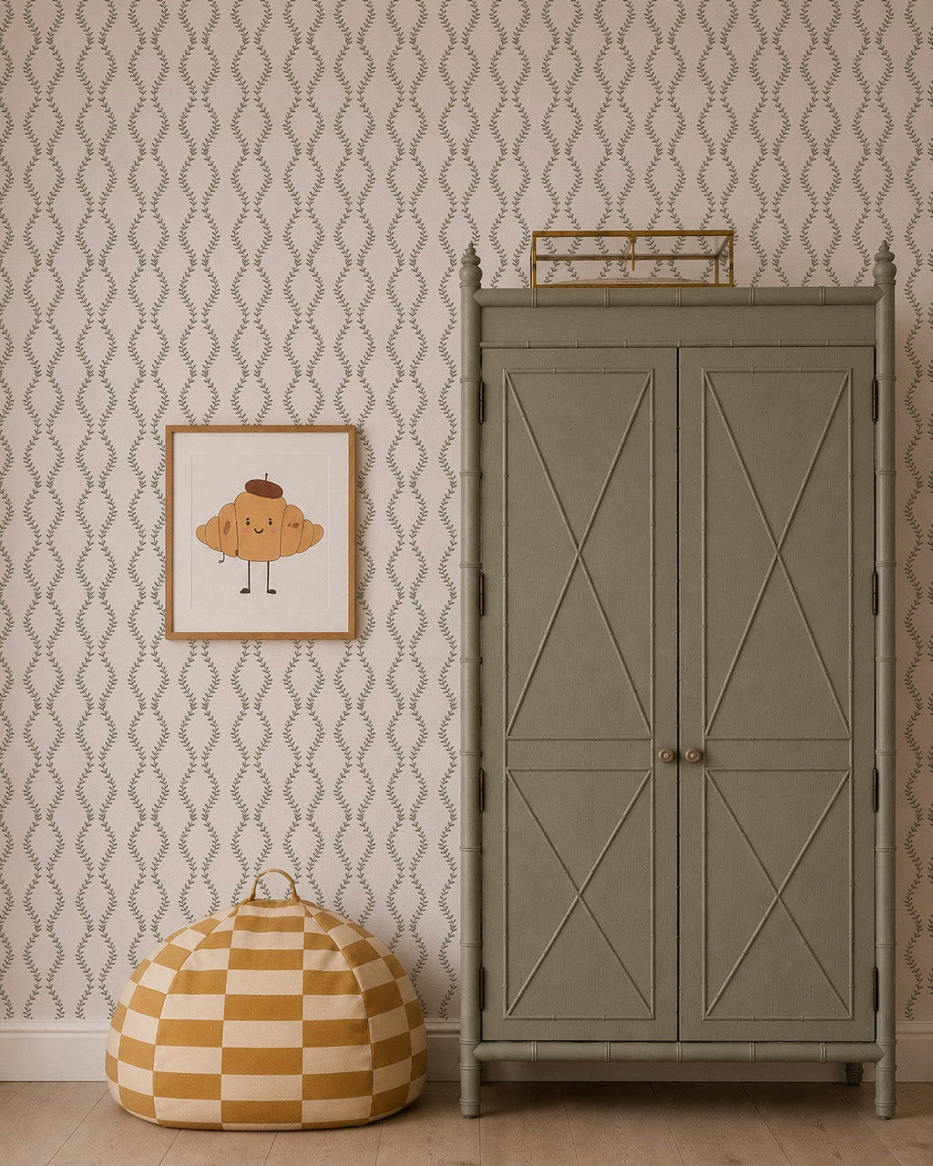 A light green armoire stands against Vintage Vines Wallpaper, accompanied by a framed croissant illustration and a yellow-and-white checkered pouf on a light wood floor.