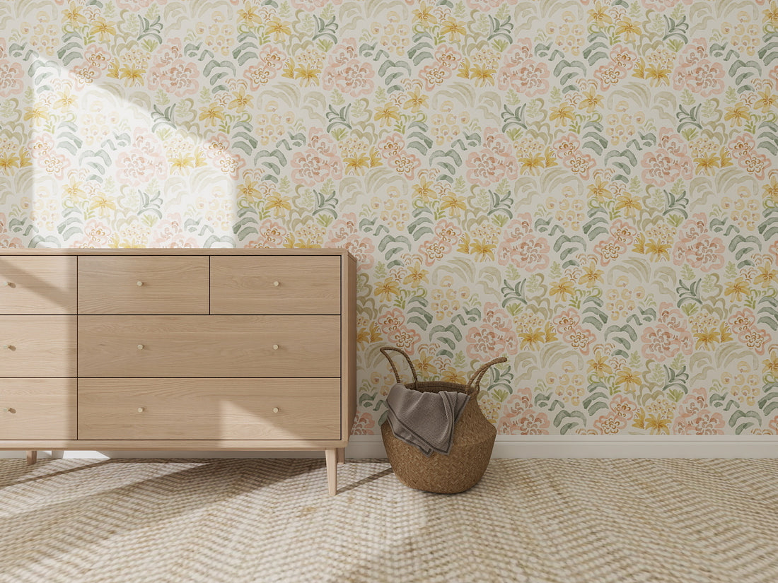 A light wooden dresser sits on a patterned carpet beside a woven basket with a blanket, backed by Floret Dreamscape Wallpaper Repeat Pattern, which adds whimsy and charm, all softly lit by natural sunlight.