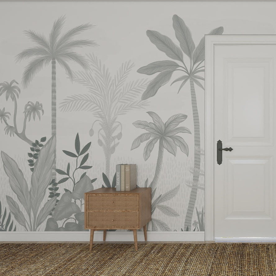 A room with a white door, wooden side table, stacked books, and the Natural Wonder Palm Wallpaper Mural Slate featuring gray tropical foliage and palm trees, finished with a woven rug for contemporary interiors.
