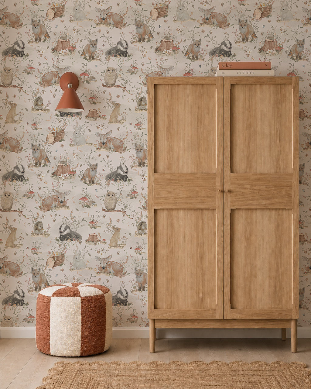 A cozy room featuring Woodland Wonder Wallpaper, a wooden wardrobe, a round brown-and-white pouf, a woven rug, and a wall sconce with a reddish shade.