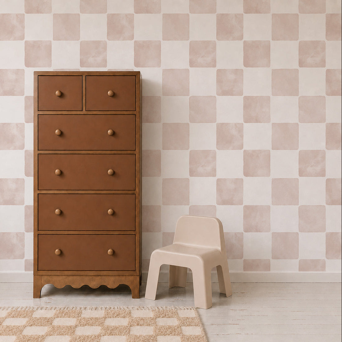 A tall wooden dresser with six drawers stands next to a small beige chair. The background showcases the Billys Checkered Wallpaper in Pink, complemented by a cream rug with a grid pattern on a white wooden floor—perfect for those who appreciate unique wall decor.
