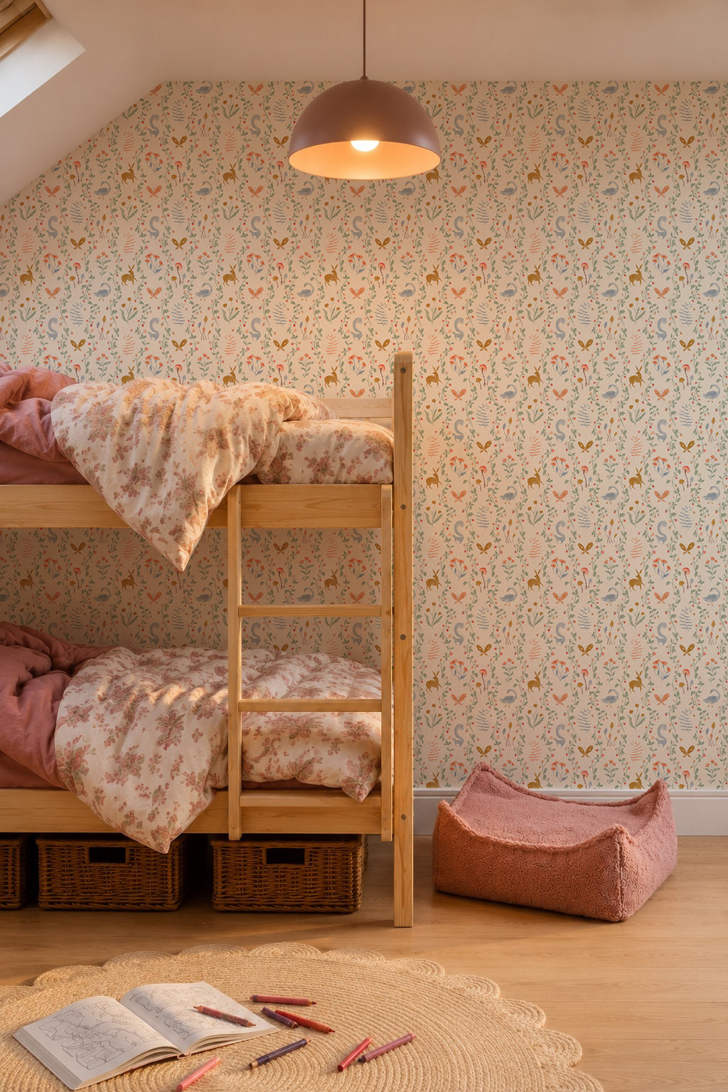 Cozy kids room with Coles Berry Patch Wallpaper, wooden bunk beds with pink bedding, a salmon dog bed, a round woven rug, crayons and paper on the floor under a hanging light.