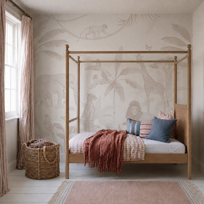 A cozy children’s room with a wooden canopy bed, pink and blue pillows, a rust-colored throw, a woven basket, and the African Safari Mural in Neutral featuring lions, giraffes, and elephants. Light streams in from a window.
