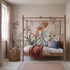 A cozy bedroom features a wooden canopy bed dressed in pastel bedding, topped with a rust-colored throw and matching pillows. The wall showcases the Quinns Flower Field Mural, bringing the vibrant look of a blooming garden indoors. Next to the window with pink curtains, a woven basket adds an extra touch of warmth.