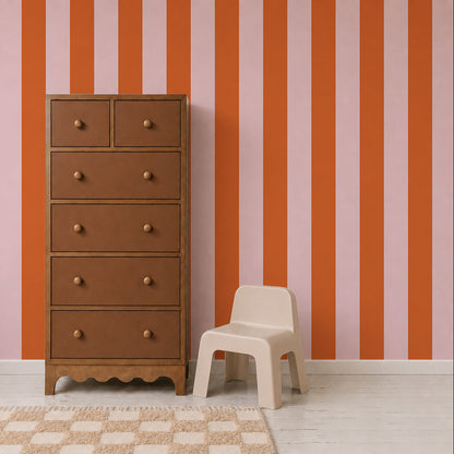 A brown wooden dresser and a small beige plastic chair sit in front of a wall adorned with Circus Stripe Wallpaper, Pink and Red. A beige checkered rug covers part of the white floor.