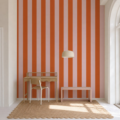 A minimalist workspace with a wooden desk and chair, a woven rug, and a pendant lamp. The wall features the Circus Stripe Wallpaper in Pink and Red, adding a playful touch to the room. A large arched window allows natural light to flood the space.