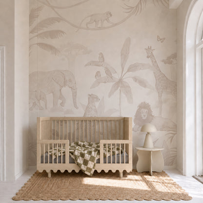 A neutral-toned children’s room features a wooden crib, checkered blanket, small chair, and a jute rug, highlighted by the African Safari Mural, Neutral—a captivating nursery wall covering adorned with elephants, giraffes, lions, and monkeys amidst lush tropical plants—creating the perfect safari-inspired effect for your little one’s space.