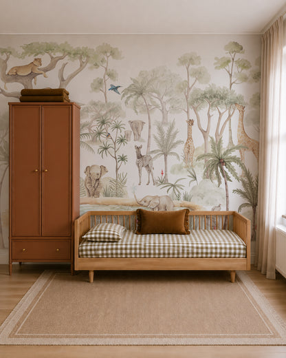 A cozy kids room features a wooden bed with gingham bedding, brown cushions, a tan rug, and a brown wardrobe. On the wall is the Safari Savannah Adventure Mural—a hand-painted nursery wallpaper of jungle animals and trees. Sunlight streams in through a window dressed with beige curtains.