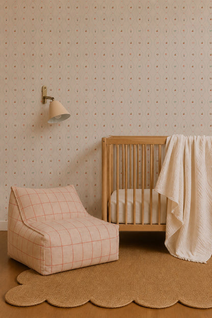 A cozy nursery featuring a wooden crib, white blanket, patterned armchair, scalloped rug, and soft beige Little Patisserie Stripe Wallpaper with subtle hand-drawn designs. A wall-mounted lamp is positioned above the crib.