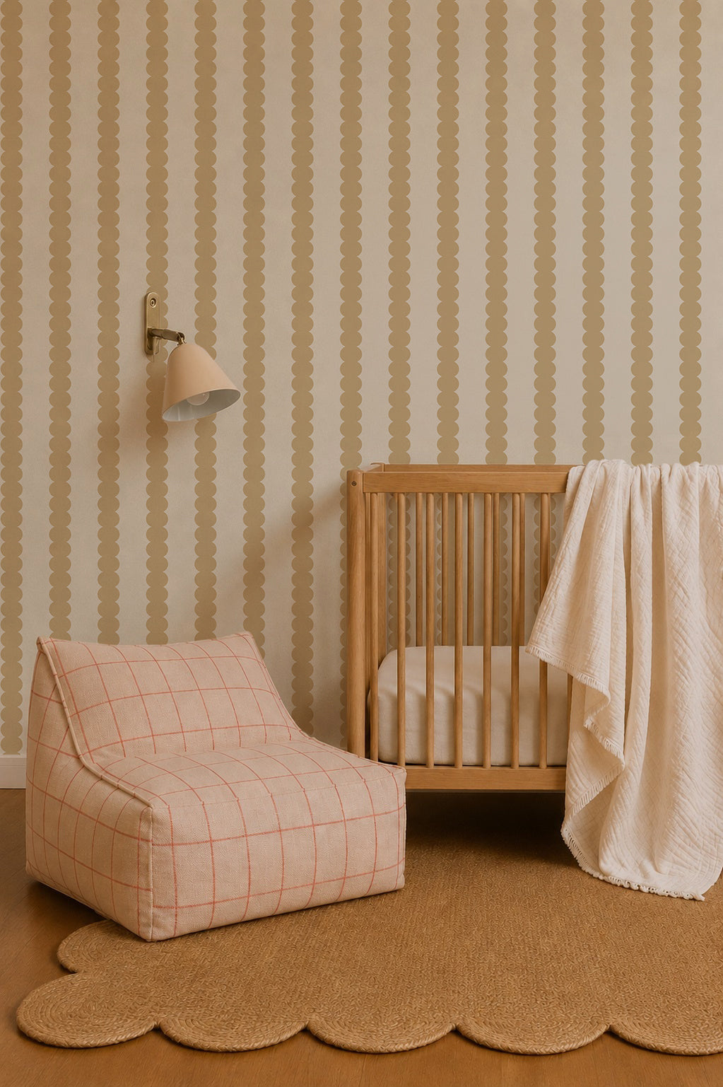 A cozy nursery with a wooden crib, a cream blanket, a checkered lounge chair, a wall lamp, Scallop Stripe Wallpaper in Yellow, and a scalloped-edge rug on a wooden floor.