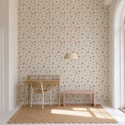 A small wooden desk and chair sit on a woven rug beside a pink bench in front of a wall adorned with the vibrant Powdered Petals Wallpaper. A round pendant lamp hangs above, and light streams in from a tall arched window.