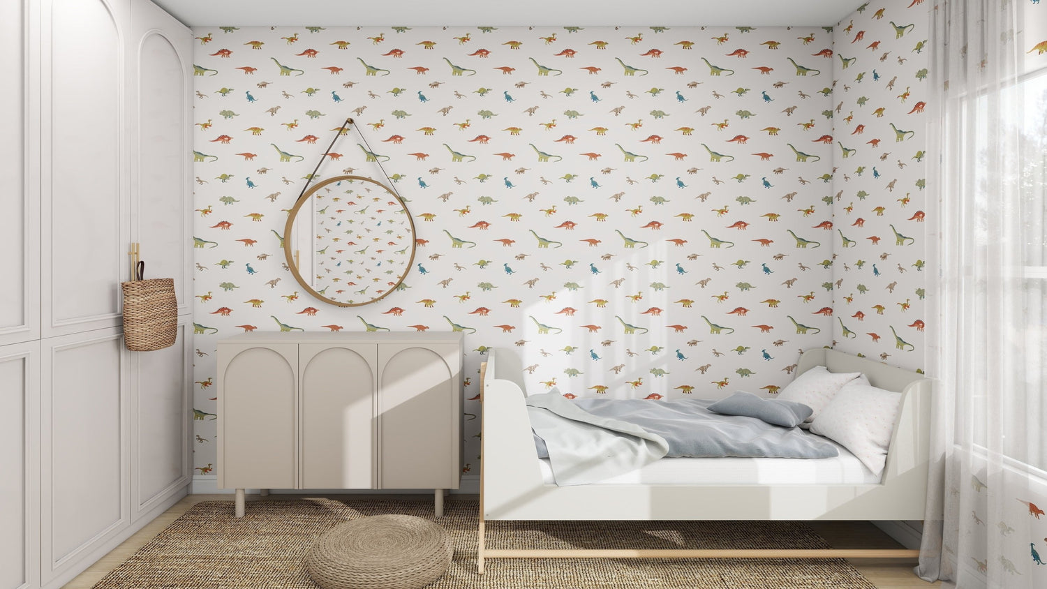 A childrens room features munks and mes Dino Discovery Repeat Wallpaper Pattern, complemented by a white bed with gray bedding, a woven rug, and a white cabinet. A round mirror reflects the adventurous design as natural light filters through sheer curtains on the window.