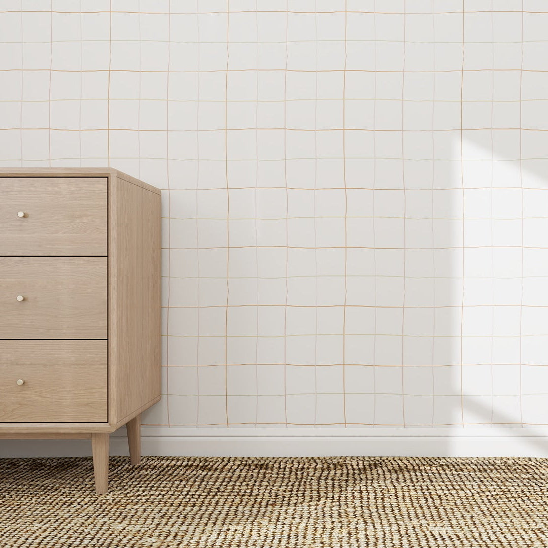 A light wood dresser with three drawers sits on a woven rug in a minimalist room. The wall behind features the Doodle Grid Wallpaper Repeat Pattern, adding subtle texture as sunlight brightens the right side.